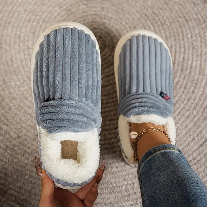 Blue-grey ribbed slippers from above, one held showing its white fleece lining and one worn with an ankle bracelet. 7
