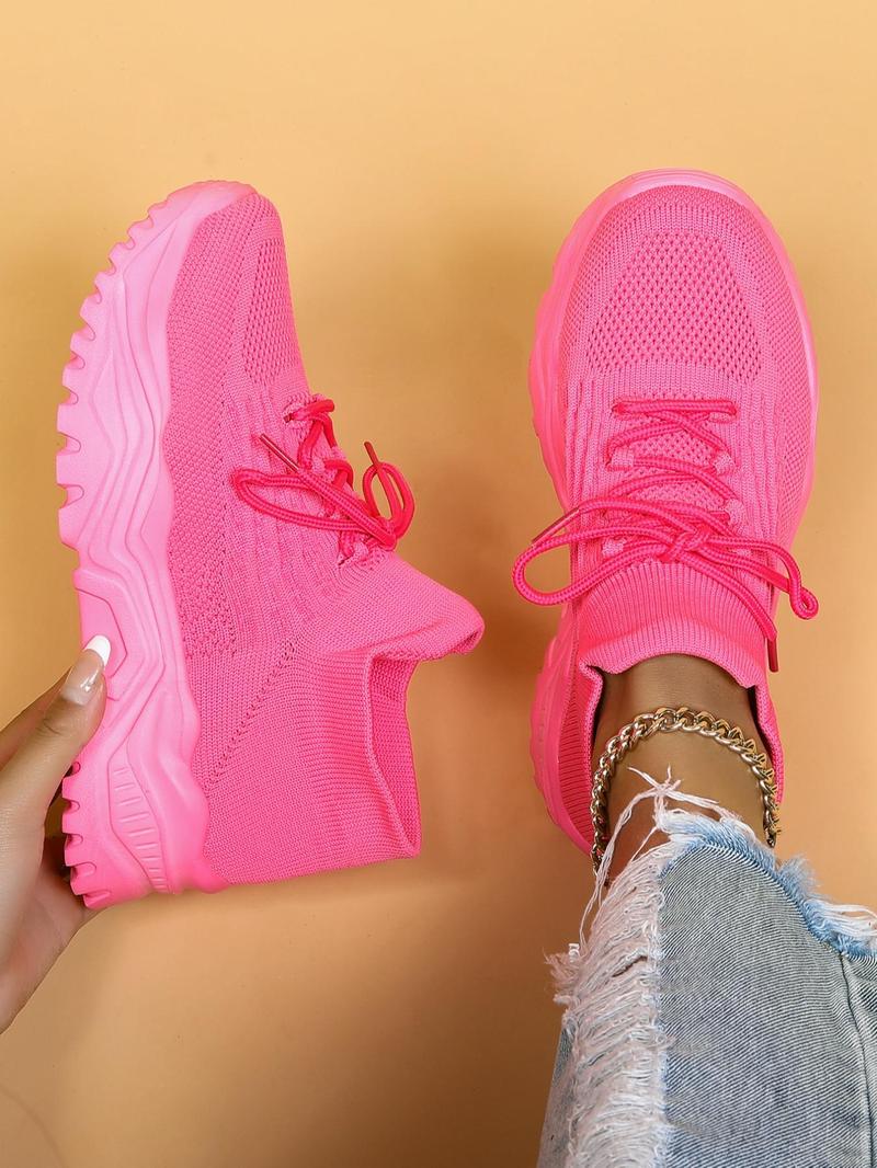 Top-down view of bright pink knit sneakers with chunky pink soles, one held in a hand and one worn with distressed jeans. 14