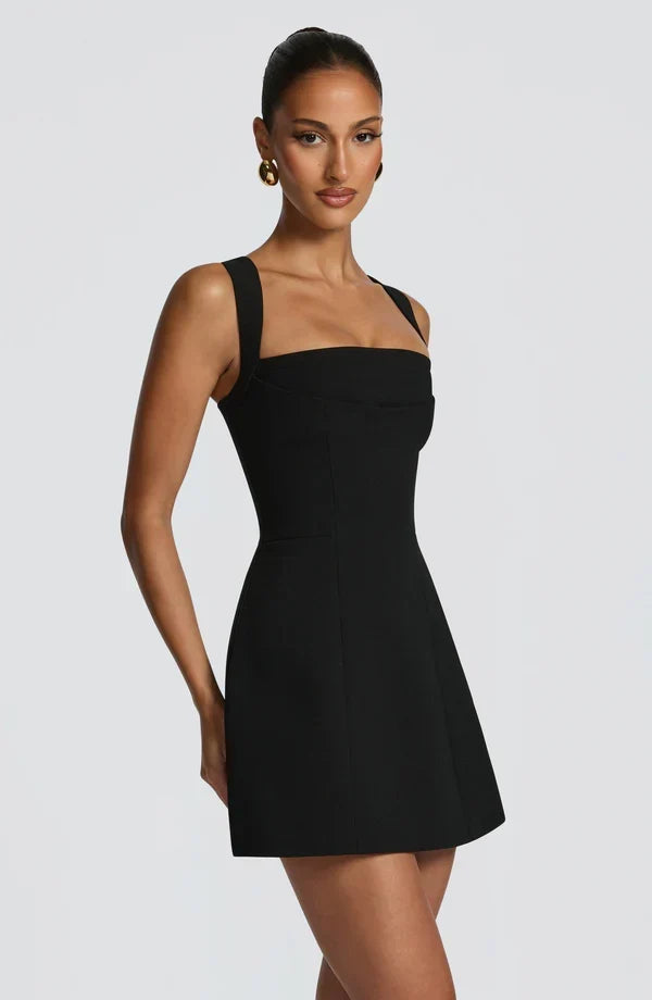 Three-quarter side view of the black mini dress, showing the structured square neckline, panelled bodice and flared skirt. 8