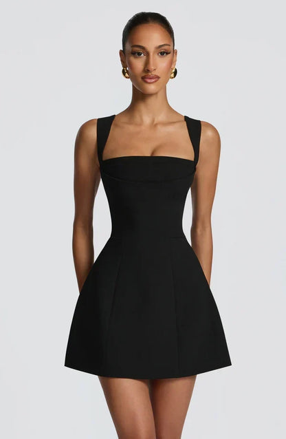 Close front view of the black mini dress on a model, showing the square neckline, wide straps and seamed corset bodice. 7