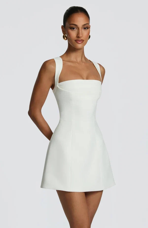 Three-quarter side view of the white mini dress, showing the structured square neckline, wide straps and seamed, flared skirt. 3