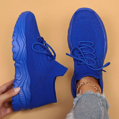 Top-down view of royal blue knit sneakers with matching chunky soles, one held up and one worn with a gold anklet. 15
