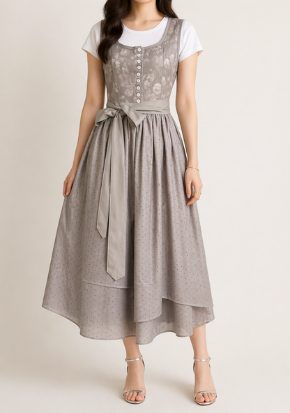 Full-length front view of the grey dirndl on a model, with silver sandals, long sash tails and a flared dotted skirt. 3