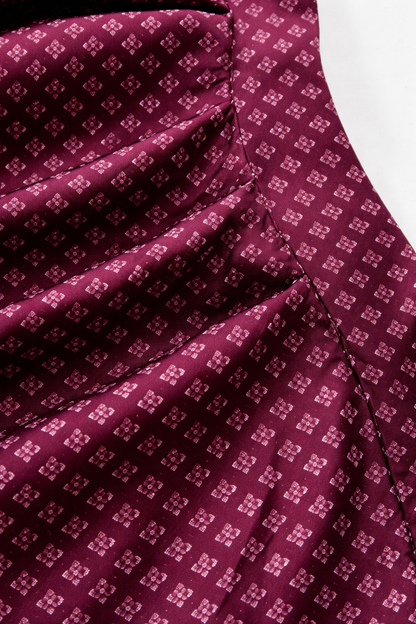 Detail of the apron fabric, a small diamond-shaped floral pattern on deep burgundy with gathered pleats and stitching. 3