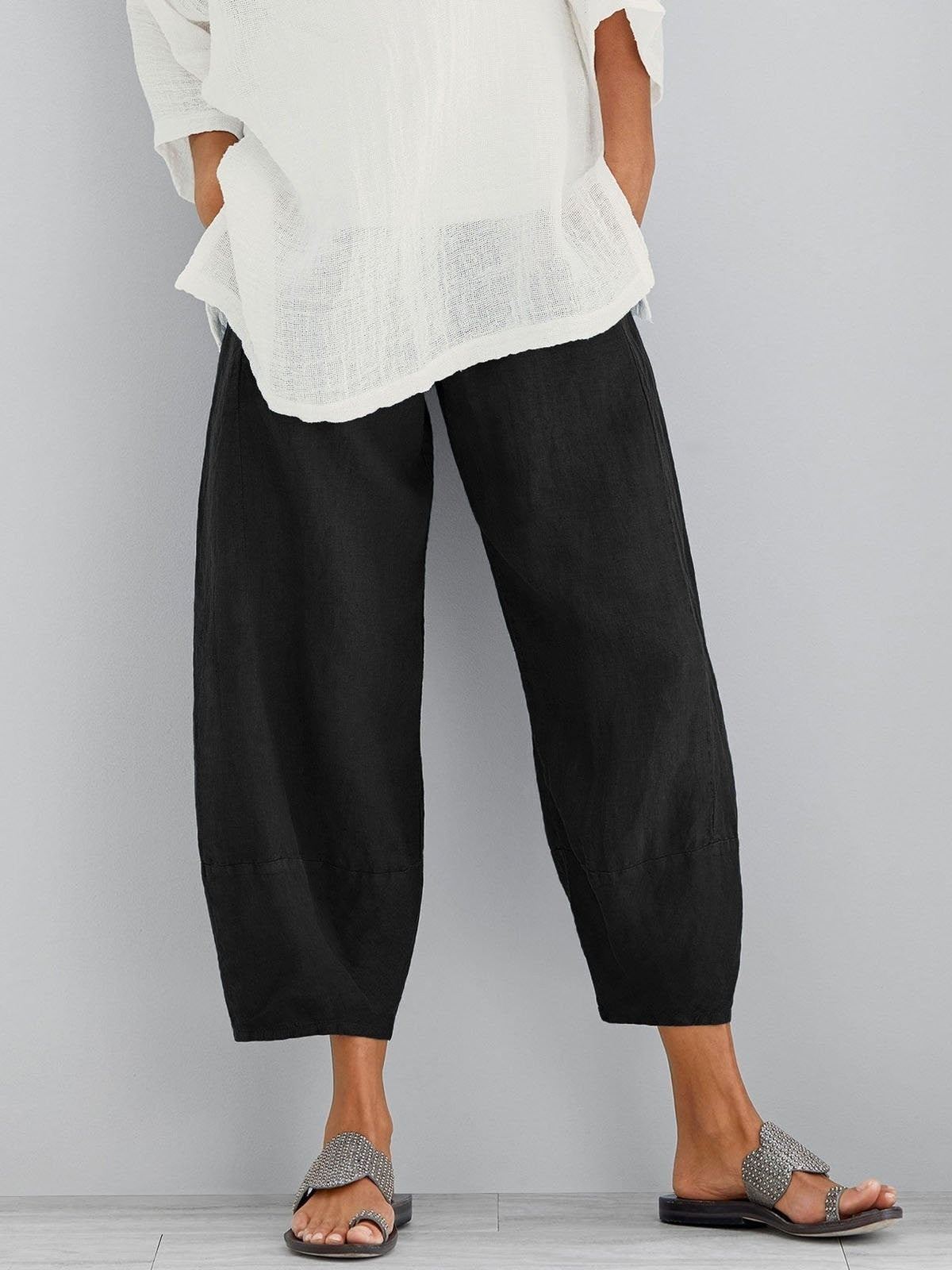 Black cropped wide-leg trousers with a gathered waist, styled with a loose white top and studded sandals. 3