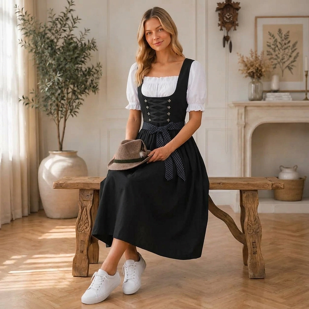 Model sits on a rustic wooden bench in the black dirndl, holding a brown felt hat with a feather in her lap. 3