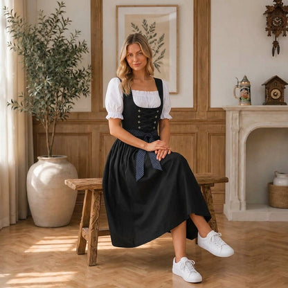 Seated three-quarter view of the dirndl on a wooden bench, showing the bodice, ribbon bow and full skirt beside a cuckoo clock. 4