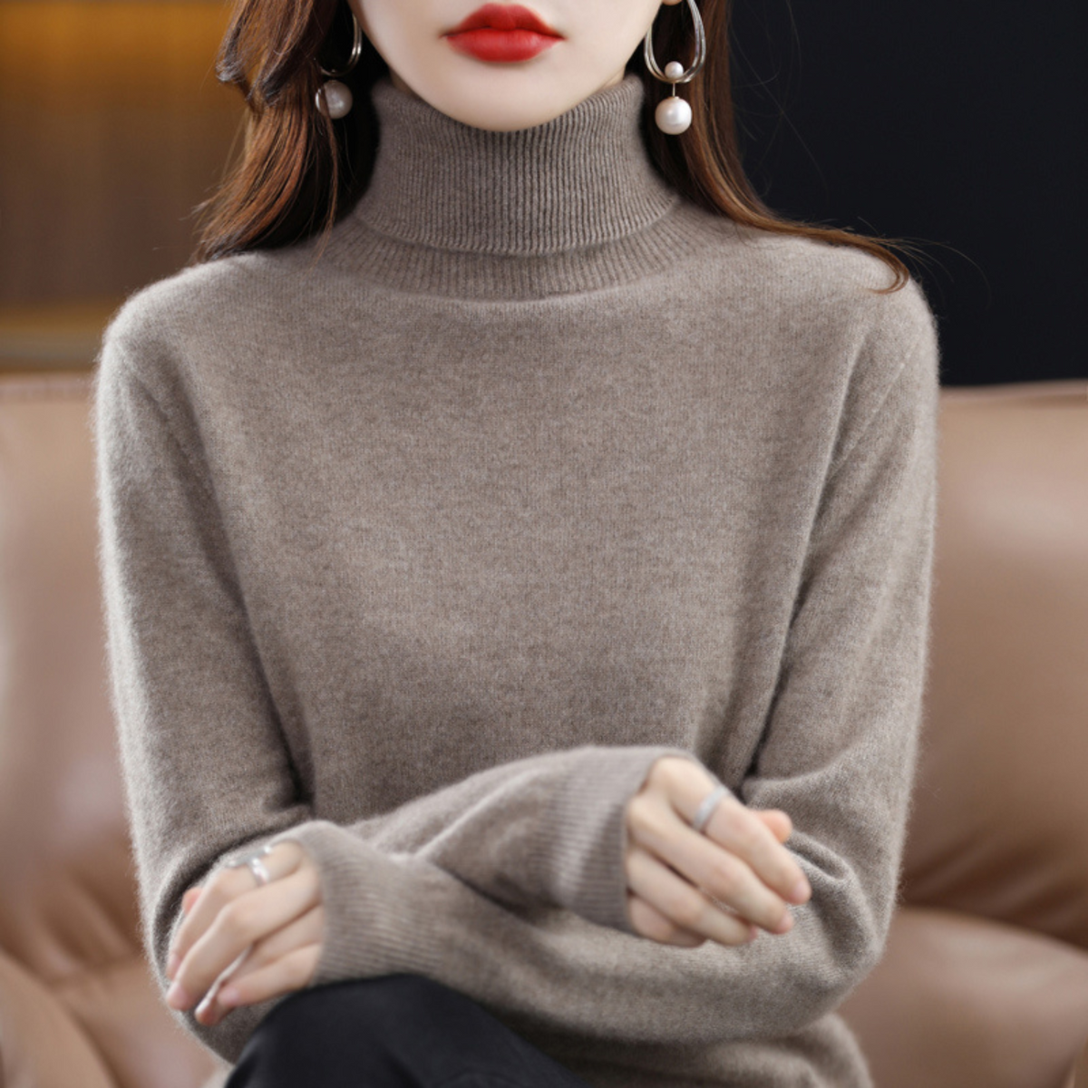 Model in the roll neck jumper in warm taupe, hands clasped, showing the thick ribbed collar and cuffs. 13