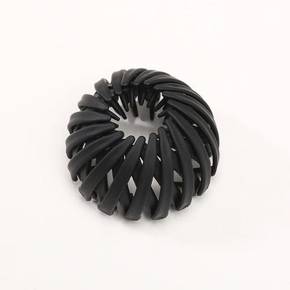 Single matte black spiral bird's-nest clip on a plain pale background, showing overlapping curved slats and inner prongs. 8