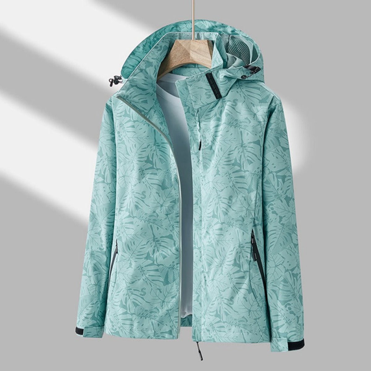 Mint green leaf-print version of the hooded jacket on a hanger, open at the front, with black pocket zips and cuff tabs. 7