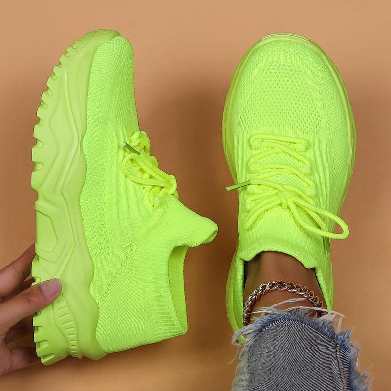 Top-down view of neon lime green knit sneakers with matching chunky soles, one held up and one worn with distressed jeans. 20