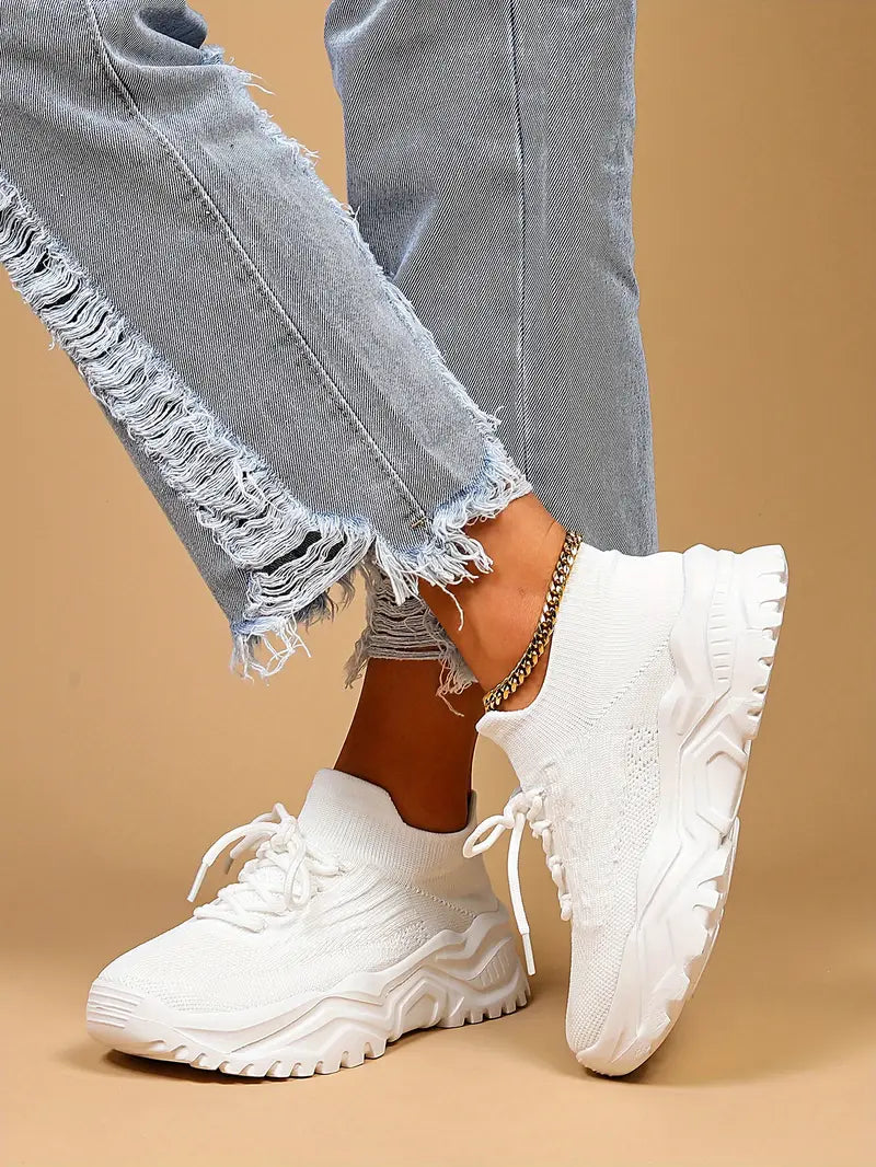 White knit lace-up sneakers with chunky white soles, worn by a model in light distressed jeans and a gold anklet. 8