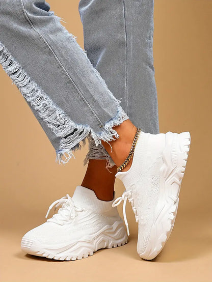 White knit lace-up sneakers with chunky white soles, worn by a model in light distressed jeans and a gold anklet. 8