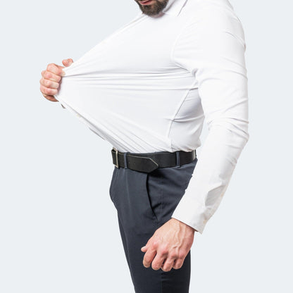 White shirt worn with navy trousers and a black belt, the model pulling the fabric away from his chest to show its stretch. 3