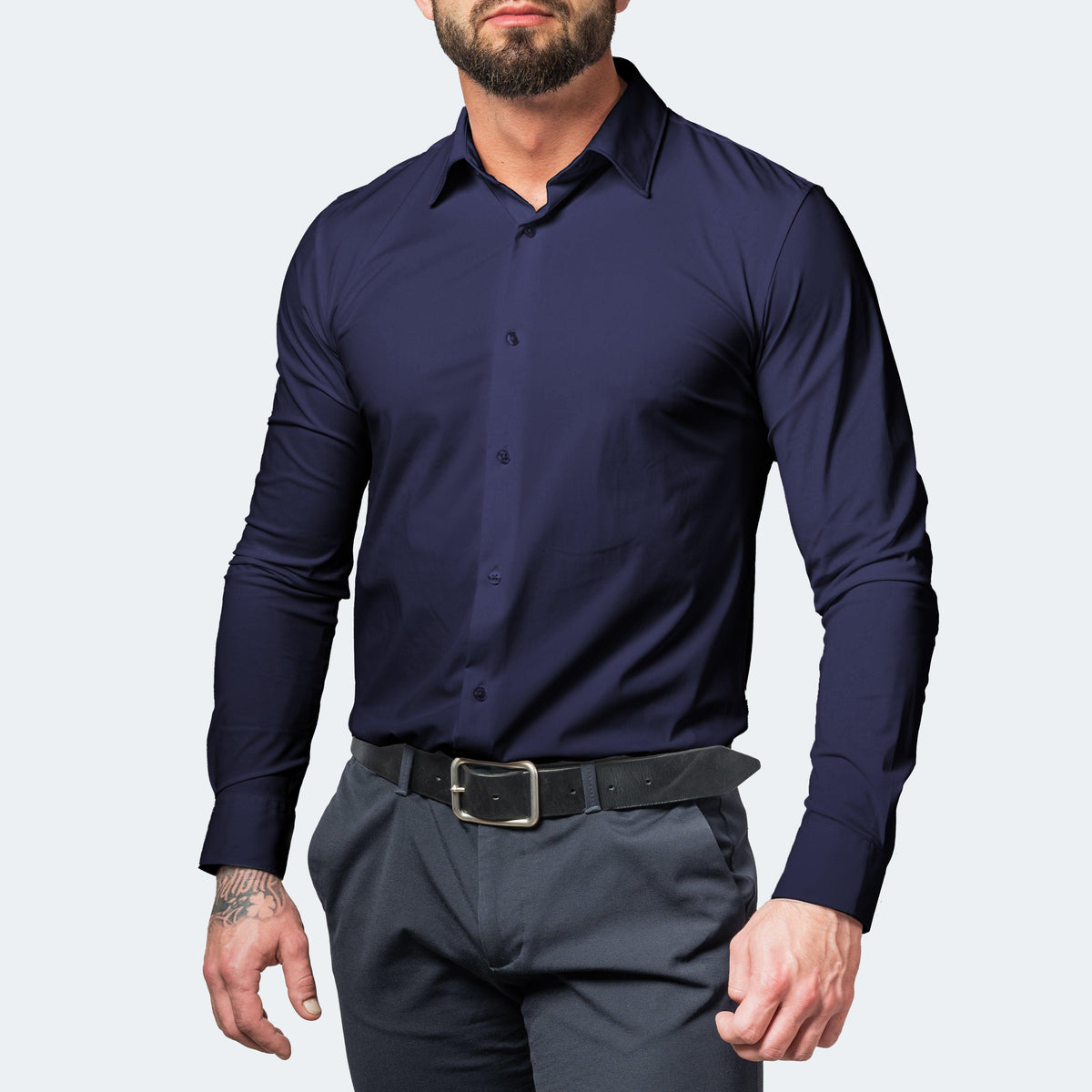 Front view of a muscular bearded model wearing a navy blue shirt buttoned up with grey trousers and a black belt. 5