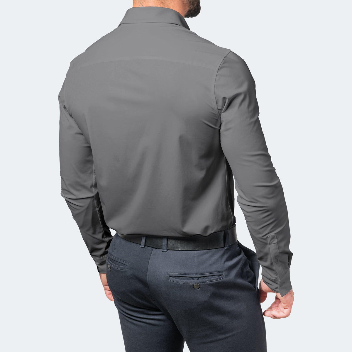 Back view of a model in a grey long-sleeved shirt with a plain yoke, tucked into navy trousers with a black belt. 6
