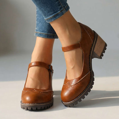Tan brown brogue Mary Jane heels with buckled ankle strap and ridged sole, worn with rolled jeans in a studio. 2