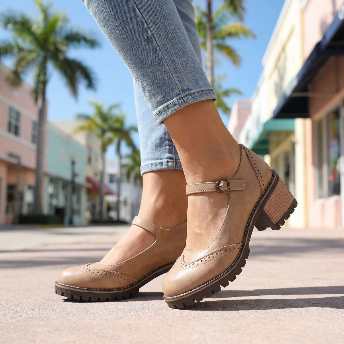 Beige Mary Jane heels with brogue toe cap and stacked heel, worn with ankle-length jeans on a sunny street. 9
