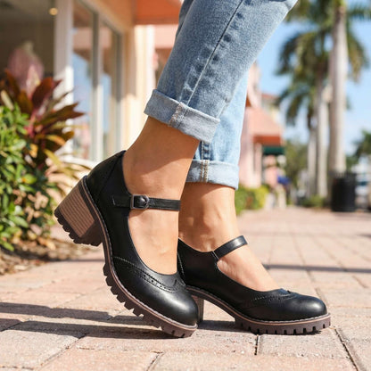 Black Mary Jane block heels with buckled ankle strap, worn with cuffed light jeans on a paved street beside palm trees. 4