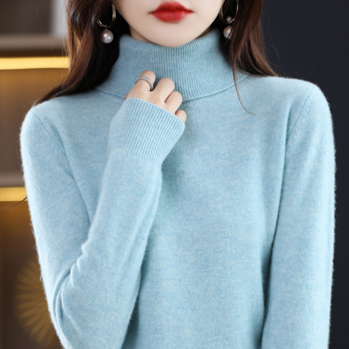Model in the roll neck jumper in pale sky blue, fingers resting at the ribbed collar, showing the ribbed cuff. 4
