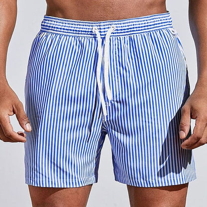 Model wearing royal blue and white vertically striped swim shorts with a white drawstring, front view with arms relaxed. 8