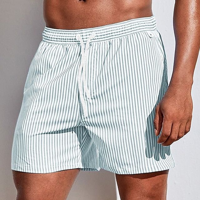 Model wearing pale grey-green and white vertically striped swim shorts with a white drawstring, one hand hanging by the side. 4