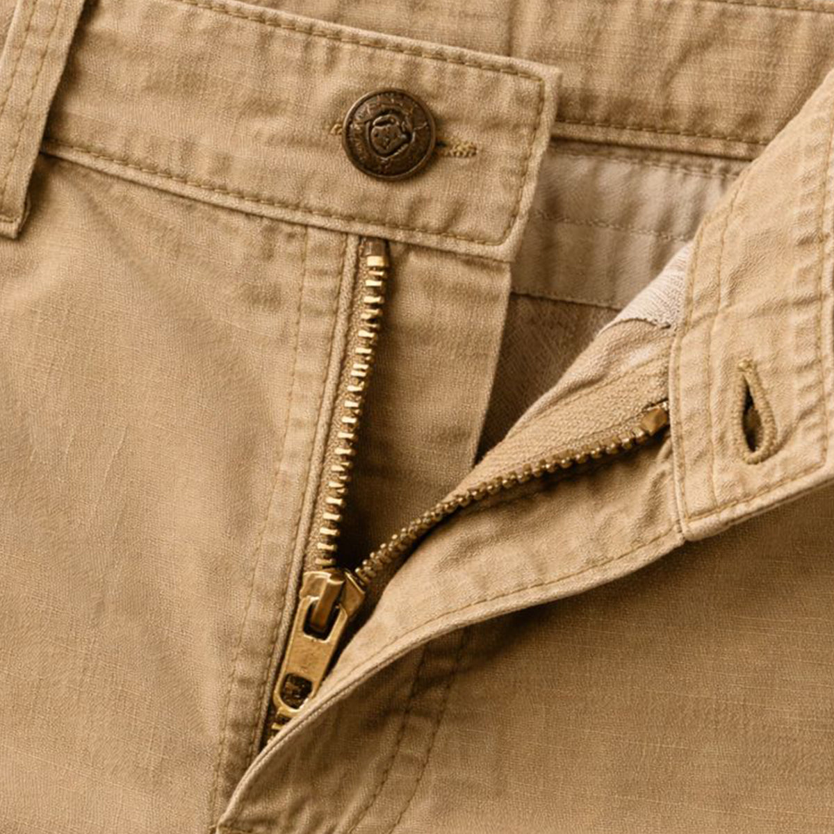 Close-up of the tan waistband, showing the metal button, brass zip partly open and the stitched fly. 6