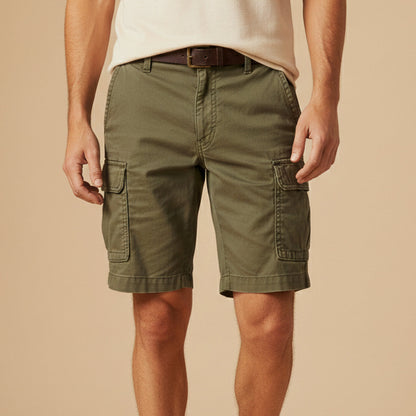 Man wearing olive green cargo shorts with a cream top and brown leather belt, hands resting by the cargo pockets. 8