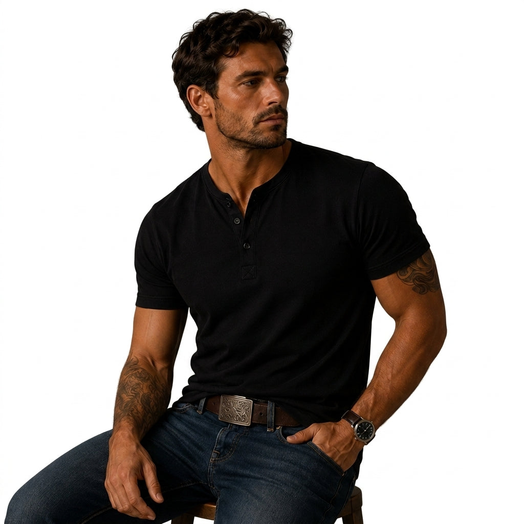 Seated man wearing the black top with blue jeans, a patterned belt buckle and visible arm tattoos 7