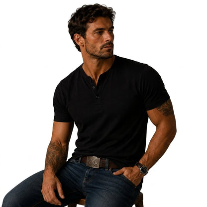 Seated man wearing the black top with blue jeans, a patterned belt buckle and visible arm tattoos 7