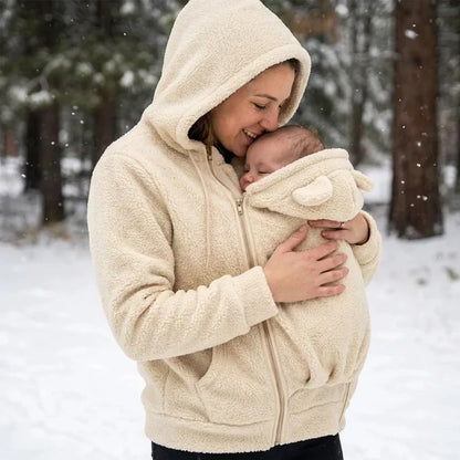 Woman in the cream fleece hoodie with hood up kissing her baby's head in the pouch, in falling snow. 16