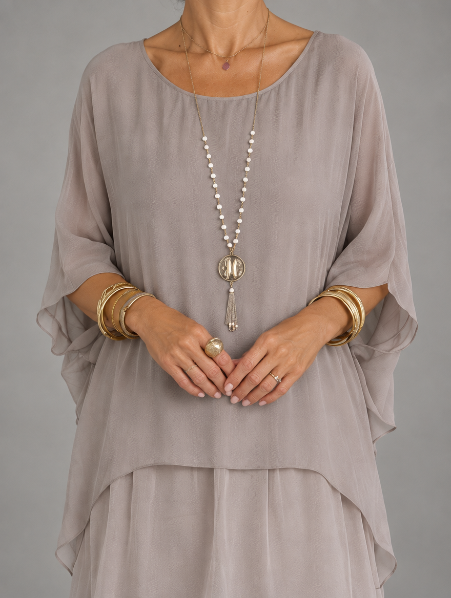Close-up of the sheer taupe chiffon overlayer with batwing sleeves, worn with a long pearl necklace and gold bangles. 21