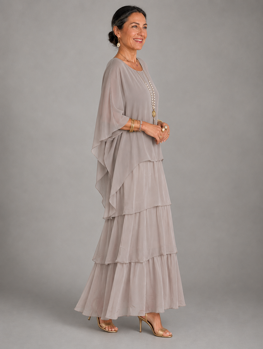 Side view of the taupe grey tiered chiffon maxi dress on a model, showing the flowing cape sleeve and layered skirt. 19