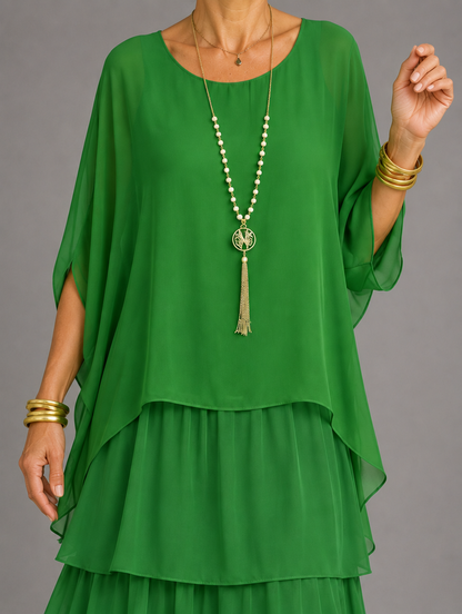 Upper body detail in green, showing the sheer cape-style top, tasselled pendant necklace and gold bangles. 33