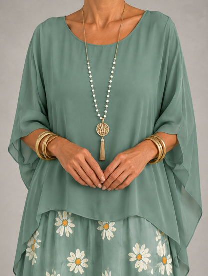 Upper body detail of the sage green chiffon top with draped sleeves, over a daisy-print skirt. 36