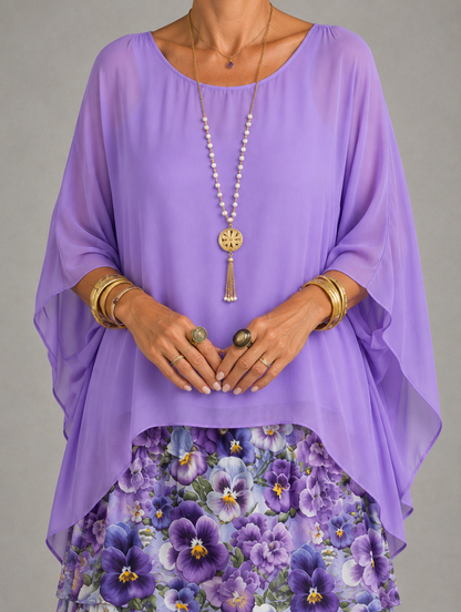 Close-up of a lilac sheer chiffon overlay with wide batwing sleeves, worn over a purple pansy-print tiered skirt. 42