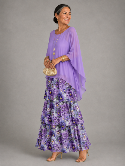 Side view of the dress with a lilac cape top over tiers printed with purple pansies, worn with a gold clutch. 40