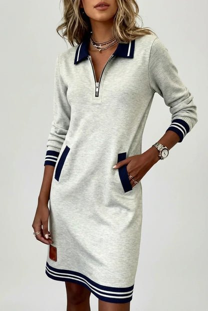 Light grey dress worn by a model against a plain background, hand in pocket, showing zip neck and striped hem. 6