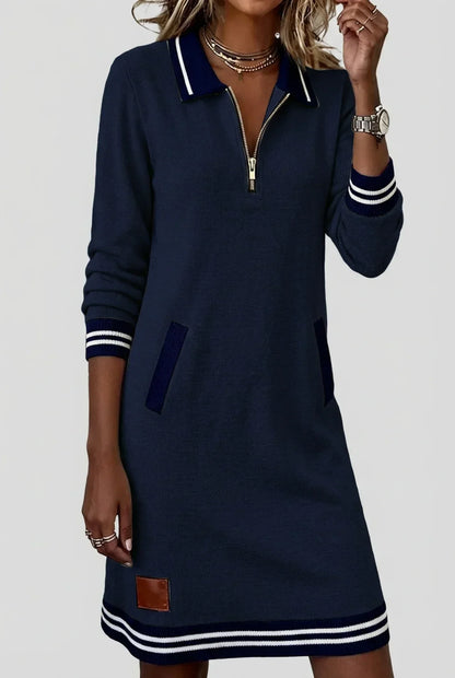 Model in the navy dress with one hand raised to her necklace, showing the knit texture, zip neck and ribbed pockets. 9