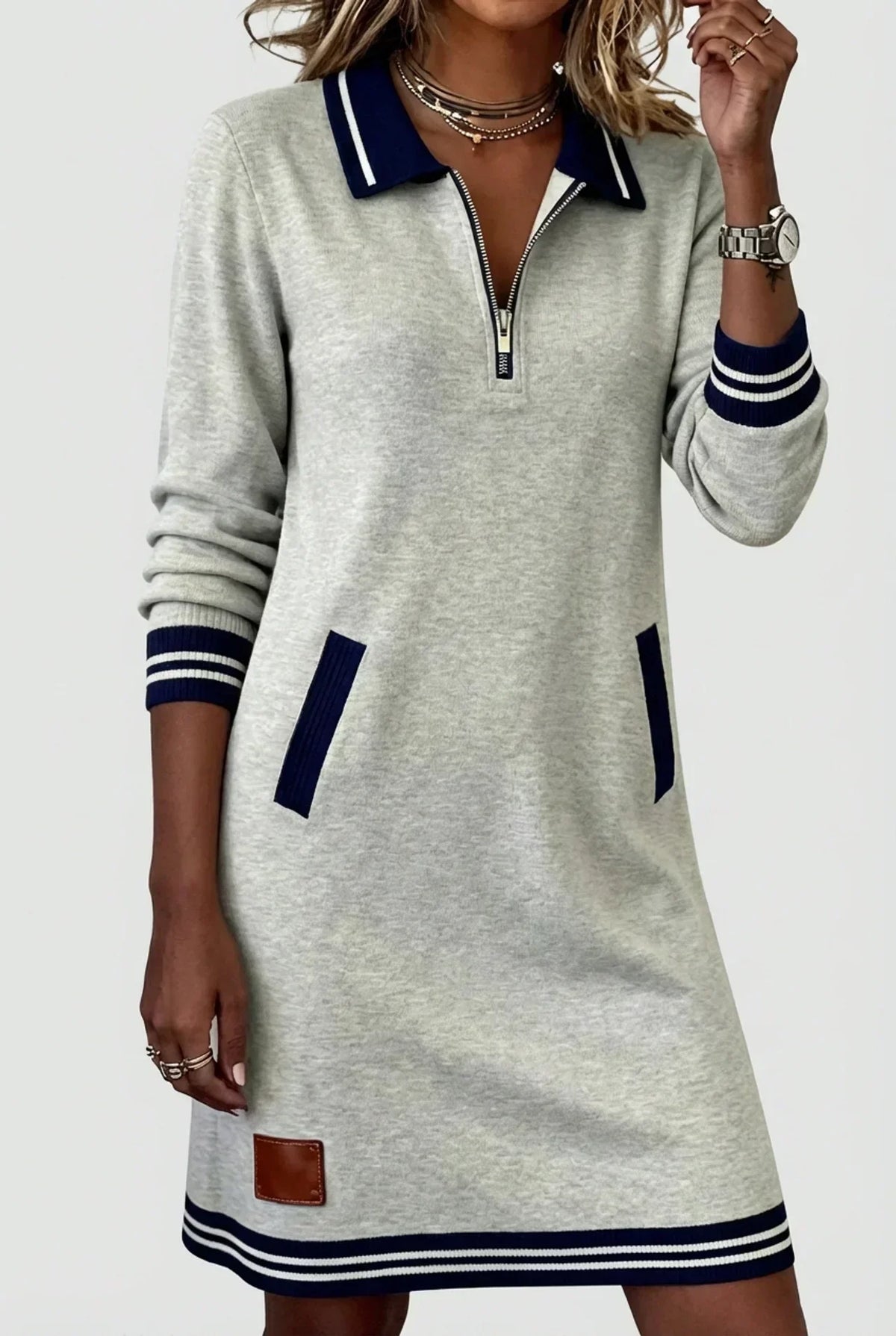 Model in the light grey marl zip-neck dress, one hand raised to her necklace, showing navy striped collar, cuffs and hem. 1