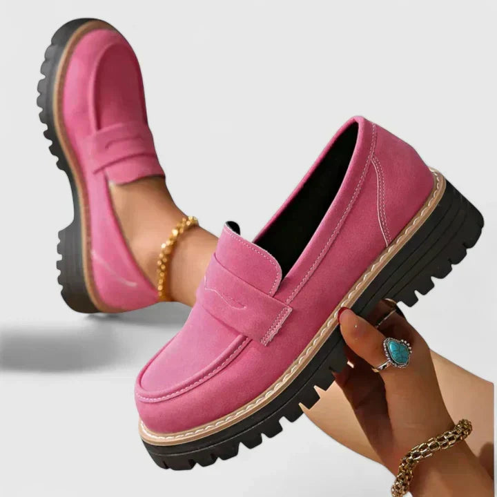 Pink loafer held up in one hand beside a worn pair, showing the thick black ridged sole and stitched strap. 2