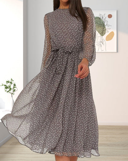 Flowing grey polka dot dress with belted waist, worn in a room with a framed botanical print and potted plant. 4