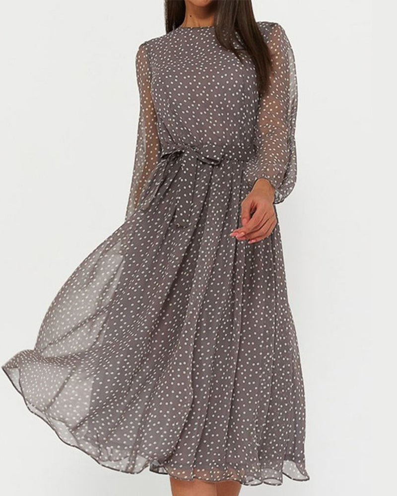 Model wearing the grey polka dot chiffon dress with sheer long sleeves and tie waist, against a plain light background. 1