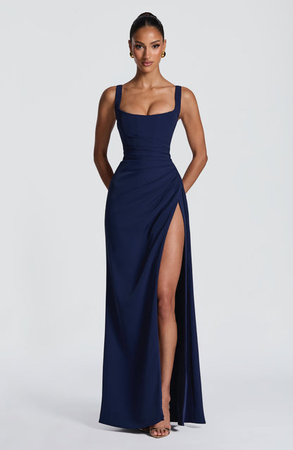 Model wearing the navy blue version of the maxi dress, front view with high slit and gold earrings. 10