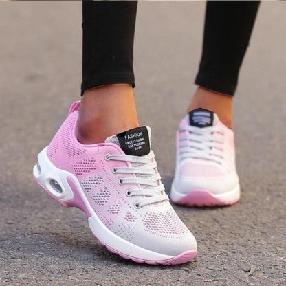 Worn on tarmac, a mesh trainer fades from soft pink to white, with pale grey laces and a pink-edged white sole. 4