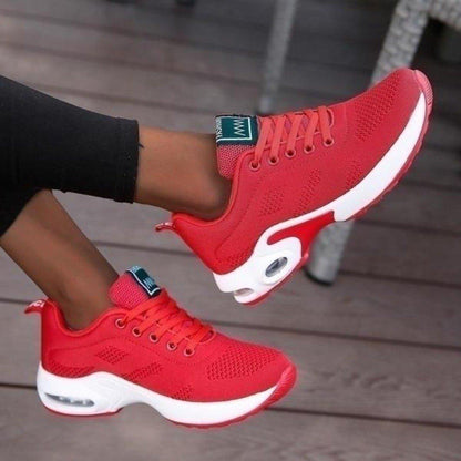 Bright red mesh trainers with a white air-cushion sole and matching red laces, shown worn with one foot raised. 7