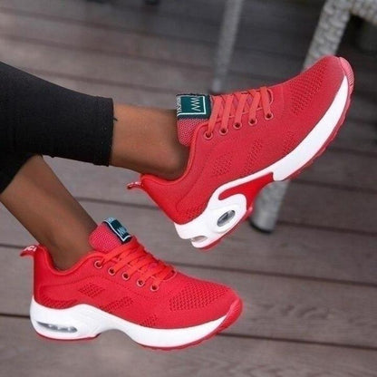 Red knit trainers with white air-cushion soles and red laces, shown from above on a model with legs crossed. 2