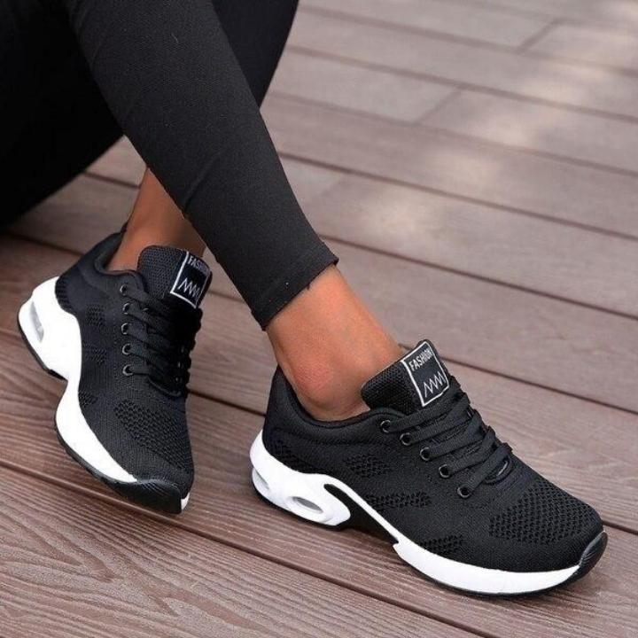 Black mesh lace-up trainers with thick white cushioned soles and visible air units, worn with black leggings on wooden decking. 1