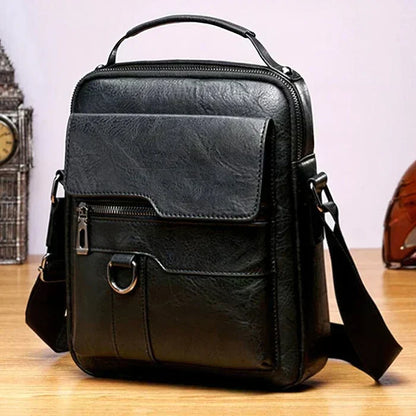 Black version of the shoulder bag with front flap pocket, zip and metal ring, standing on a wooden table. 3