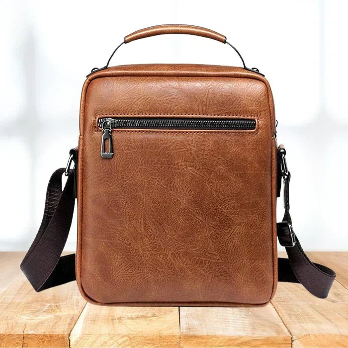Back of the tan shoulder bag, showing a single zipped pocket, top carry handle and strap attachments. 6